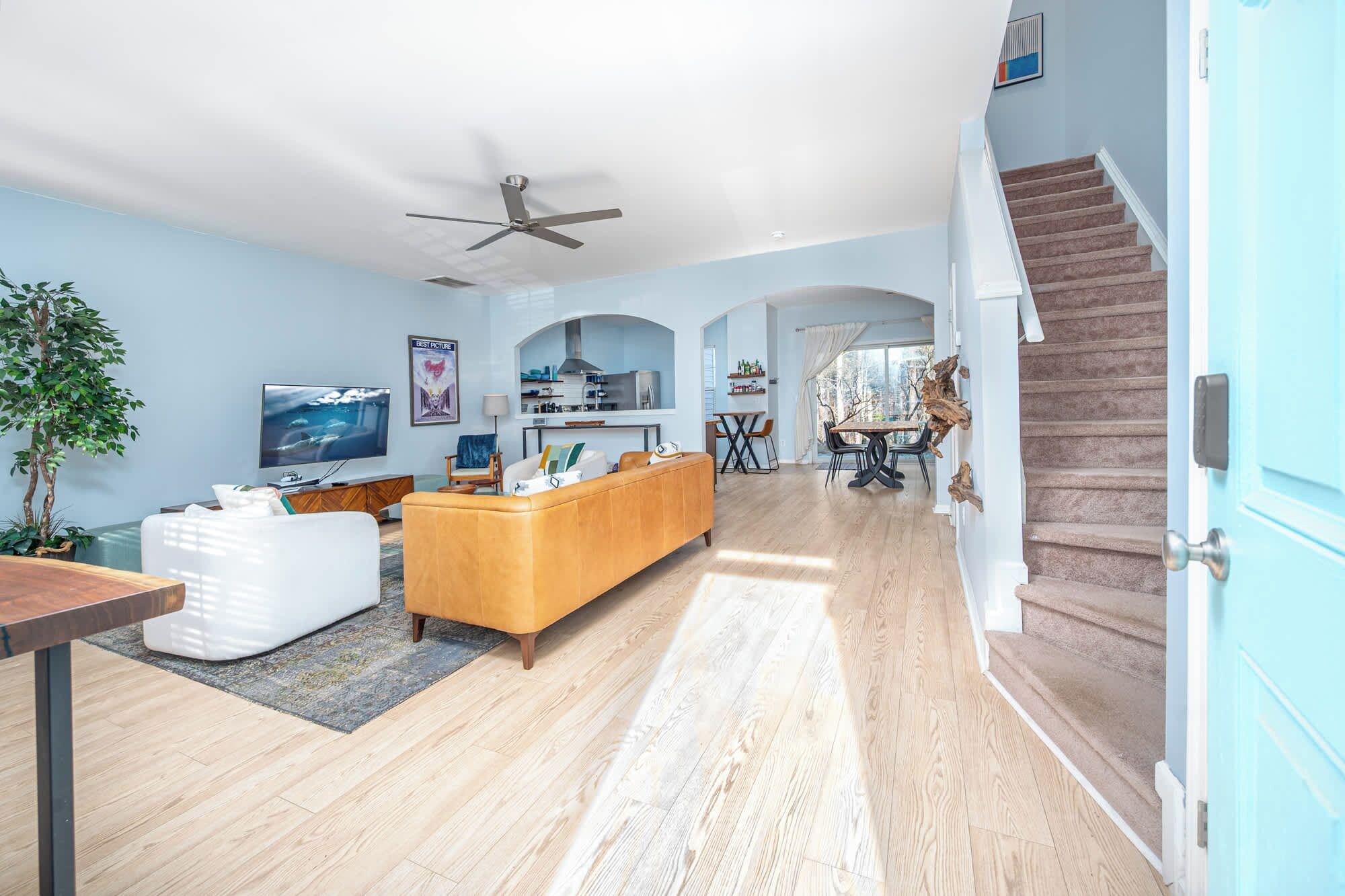 A spacious living room with a large TV, a sofa, and a dining area with a table and chairs. There is a staircase leading to another level.