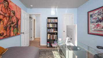 A bedroom with a bed, a bookshelf, a desk with a computer, and a large painting on the wall.