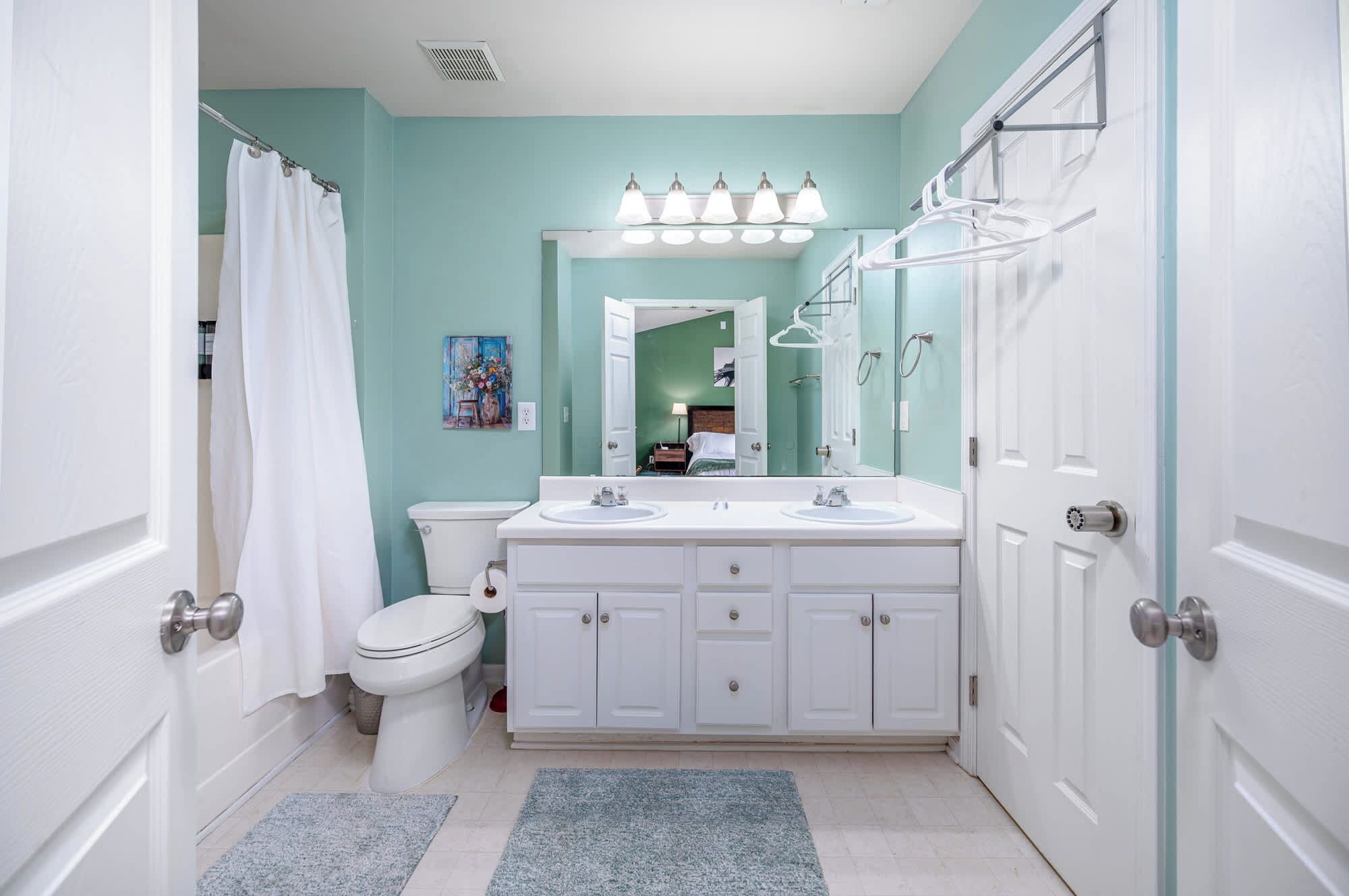 A bathroom with a white toilet, double sinks, a mirror, and a shower area.