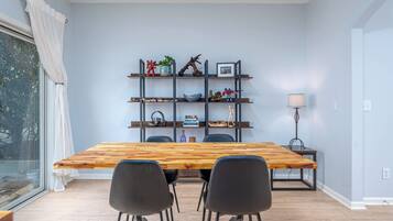 Ein Essbereich mit einem Holztisch, vier schwarzen Stühlen, einem Metallregal mit verschiedenen Gegenständen und einer Stehlampe.