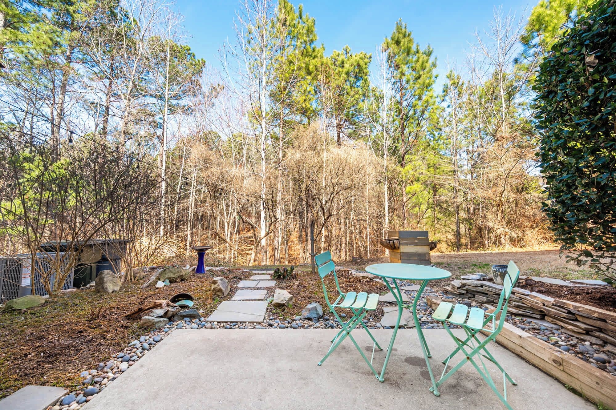 An outdoor patio area with a concrete floor, a round table, and two green folding chairs.