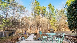An outdoor patio area with a concrete floor, a round table, and two green folding chairs. - Modern 3-br Townhome w Private Backyard Near RTP (Morrisville)