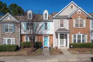 A row of townhouses with a central entrance, brick and stone facades, and a tree in the front yard. - Modern 3-br Townhome w Private Backyard Near RTP (Morrisville)