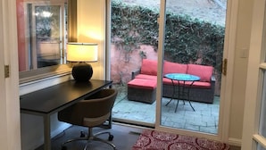Et værelse med skrivebord, stol og en skydedør til en udendørs terrasse med en rød sofa og et bord.