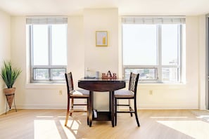 A dining area with a dark wooden table, two chairs, a potted plant, and a window with blinds.
