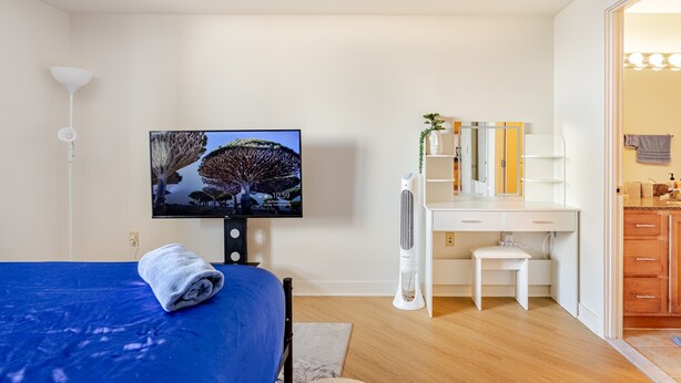 A bedroom with a bed, a TV, a desk, and a bathroom visible through an open door. - Downtown Silver Spring 2BR Skyline Balcony Suite Walkable to DC Metro Luxepad (Silver Spring)