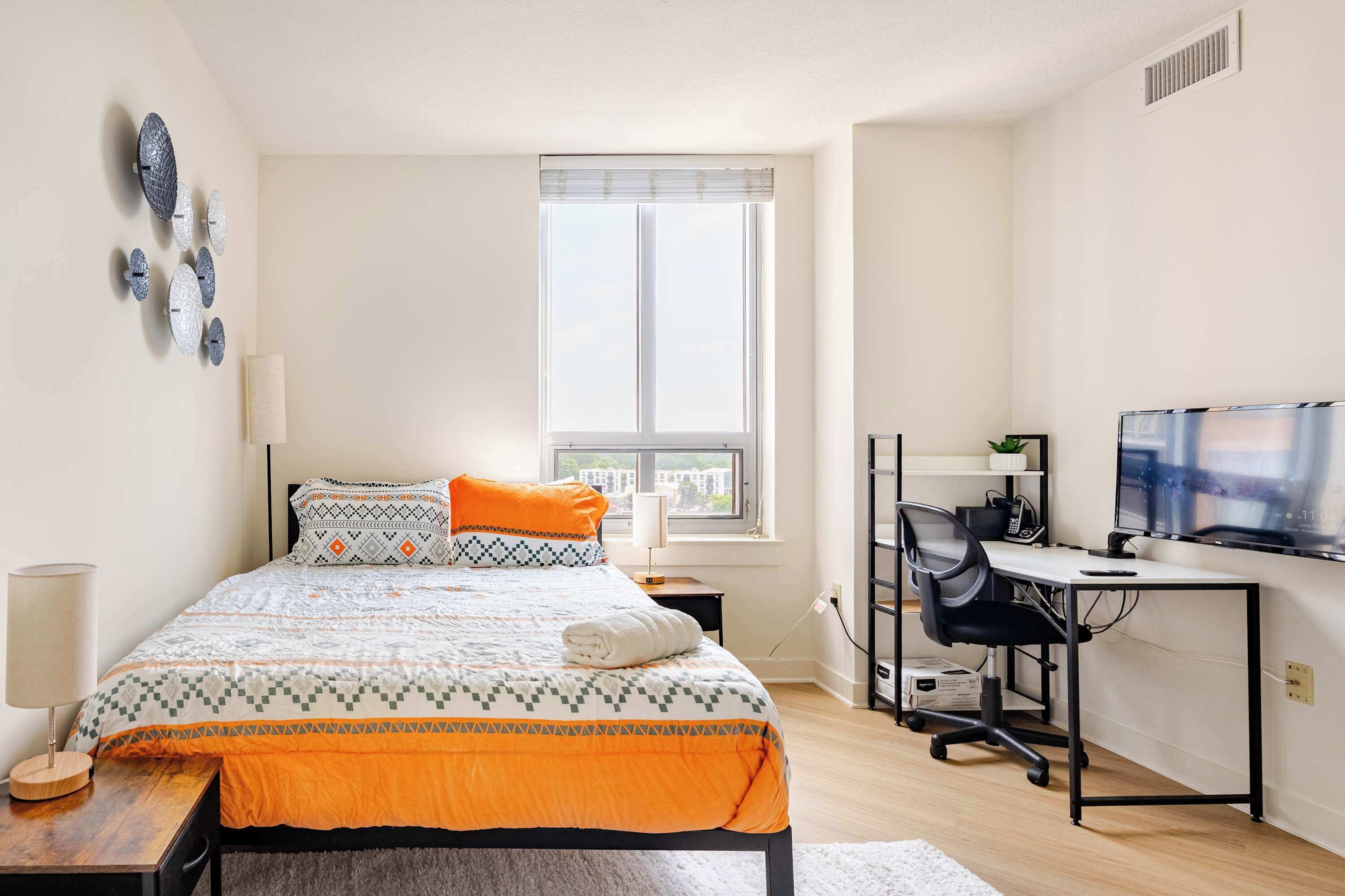 Un dormitorio con cama, escritorio, televisor y ventana.