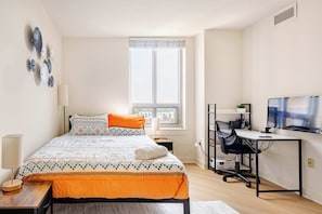 A bedroom with a bed, a desk, a TV, and a window.