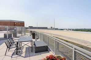 Una terraza en la azotea con mobiliario exterior, un contenedor de basura y vistas de la ciudad.