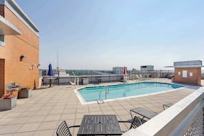 A rooftop pool with a view of the city skyline, outdoor seating, and a brick building.