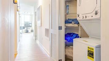 A laundry room with a dryer and washing machine, a hallway with wooden flooring, and a door leading to another room.