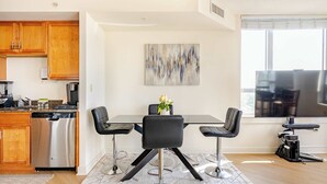 A modern kitchen with wooden cabinets, a stainless steel dishwasher, and a dining area with a glass table and black chairs. - Downtown Silver Spring 2BR Skyline Balcony Suite Walkable to DC Metro Luxepad (Silver Spring)