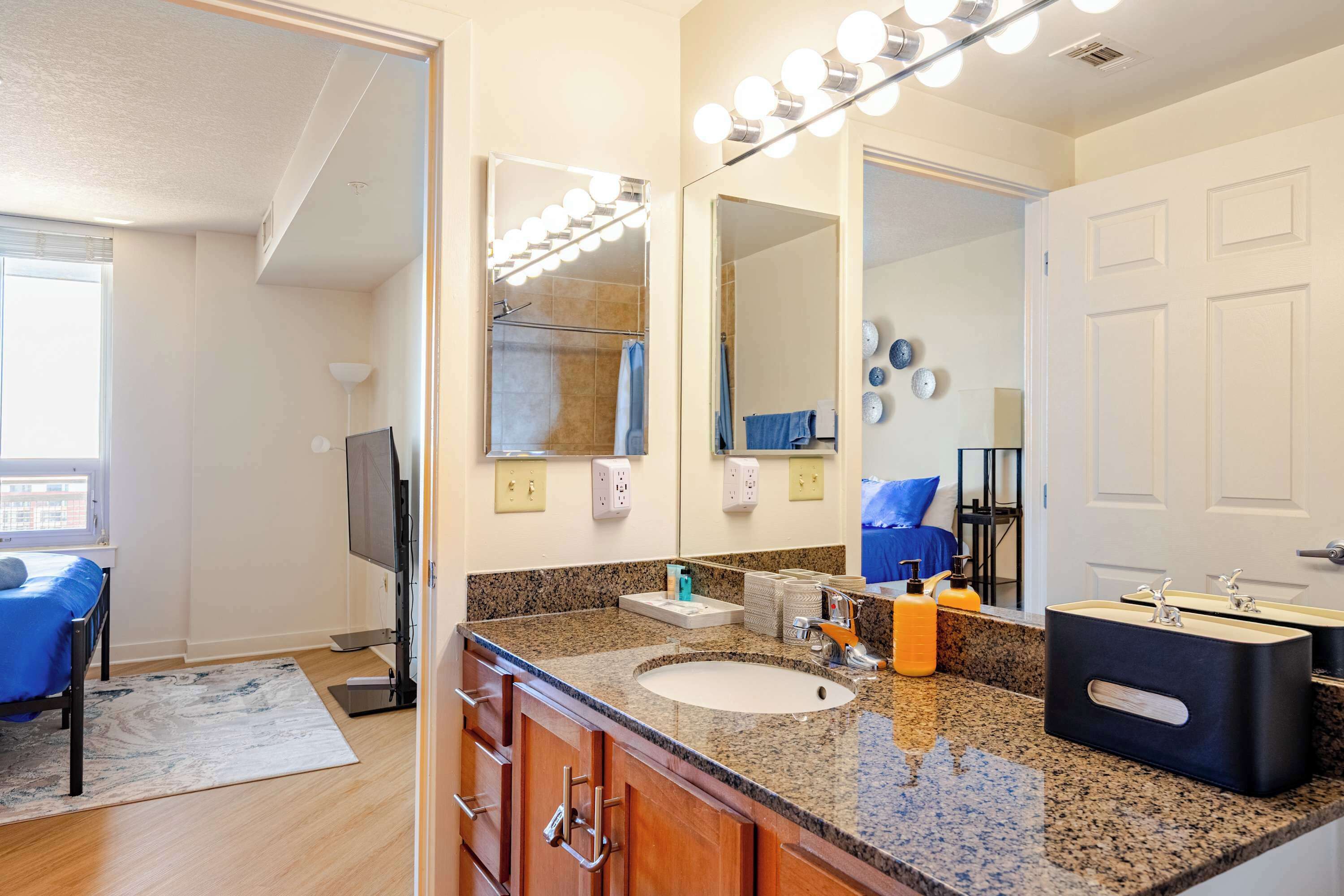 A bathroom with a large mirror, vanity, sink, and lights.