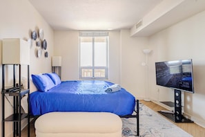 Um quarto com uma cama, televisão, janela e mesa de cabeceira.