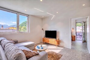 A modern living room with a sofa, a coffee table, and a TV on a wooden stand. - Urban Maggiolina Sunset with Terrace & Mountain Views, Locarno, Switzerland (Locarno)