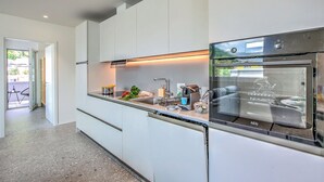 Ett modernt kök med en inbyggd ugn, en diskmaskin och en bänkskiva med olika köksredskap.