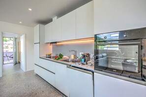 A modern kitchen with a built-in oven, a dishwasher, and a countertop with various kitchen items. - Urban Maggiolina Sunset with Terrace & Mountain Views, Locarno, Switzerland (Locarno)