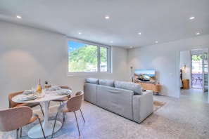 A modern living room with a grey sectional sofa, a dining table with chairs, and a television on a wooden stand. - Urban Maggiolina Sunset with Terrace & Mountain Views, Locarno, Switzerland (Locarno)