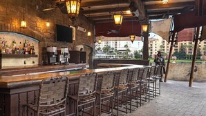 A bar area with a stone wall, hanging lights, and a view of buildings in the background. - Spend the 4th of July at the beautiful Bonnet Creek Reaort in Orlando Florida (Lake Buena Vista)