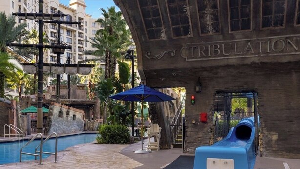 A swimming pool area with a slide, lounge chairs, and a building labeled 'TRIBULATION.' - Spend the 4th of July at the beautiful Bonnet Creek Reaort in Orlando Florida (Lake Buena Vista)