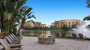 A fire pit surrounded by Adirondack chairs, a pond, and a building complex in the background. - Spend the 4th of July at the beautiful Bonnet Creek Reaort in Orlando Florida (Lake Buena Vista)