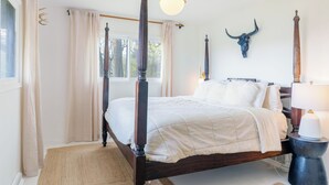 Una cama con dosel de estructura oscura, una decoración de cráneo de toro colgado en la pared, una lámpara de noche y una ventana con cortinas.