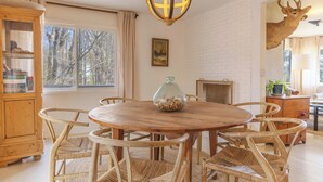 Comedor con una mesa redonda de madera, sillas de mimbre, un aparador de madera y un trofeo de cabeza de ciervo en la pared.