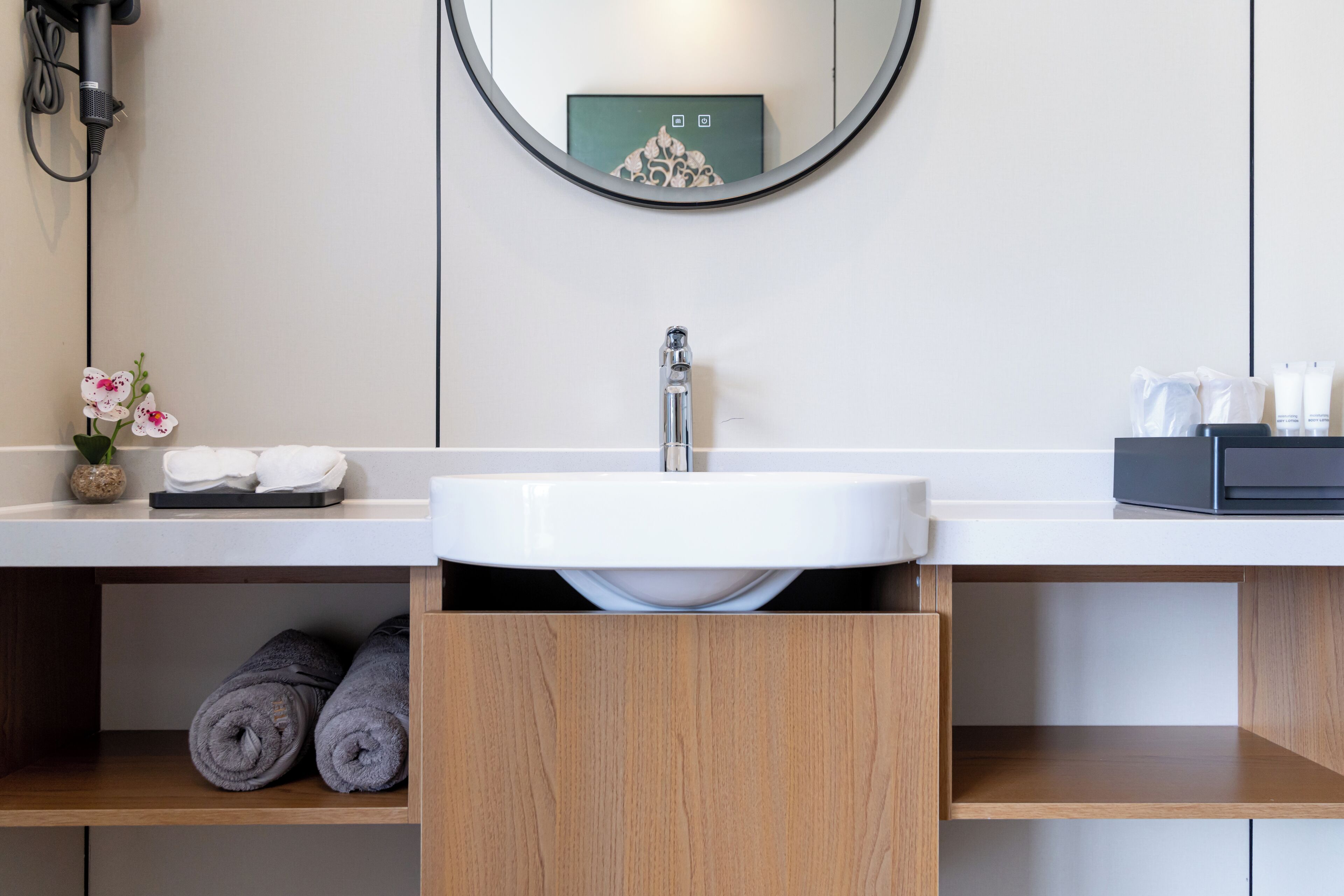 A modern bathroom with a white sink, wooden shelves, a mirror, and a towel rack.
