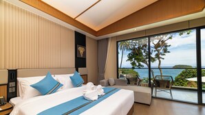 Une chambre d’hôtel moderne, dotée d’un grand lit, d’un canapé, d’un balcon avec vue sur la mer et d’un téléphone sur la table de chevet.