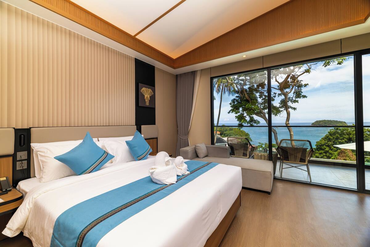 Una habitación de hotel moderna con una cama grande, un sofá, un balcón con vistas al mar y un teléfono en la mesita de noche.