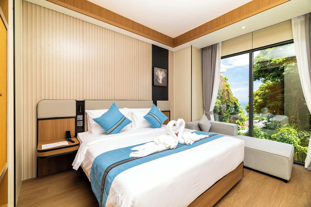 Una habitación de hotel moderna con una cama grande, una mesita de noche y vistas a zonas verdes a través de un ventanal amplio.