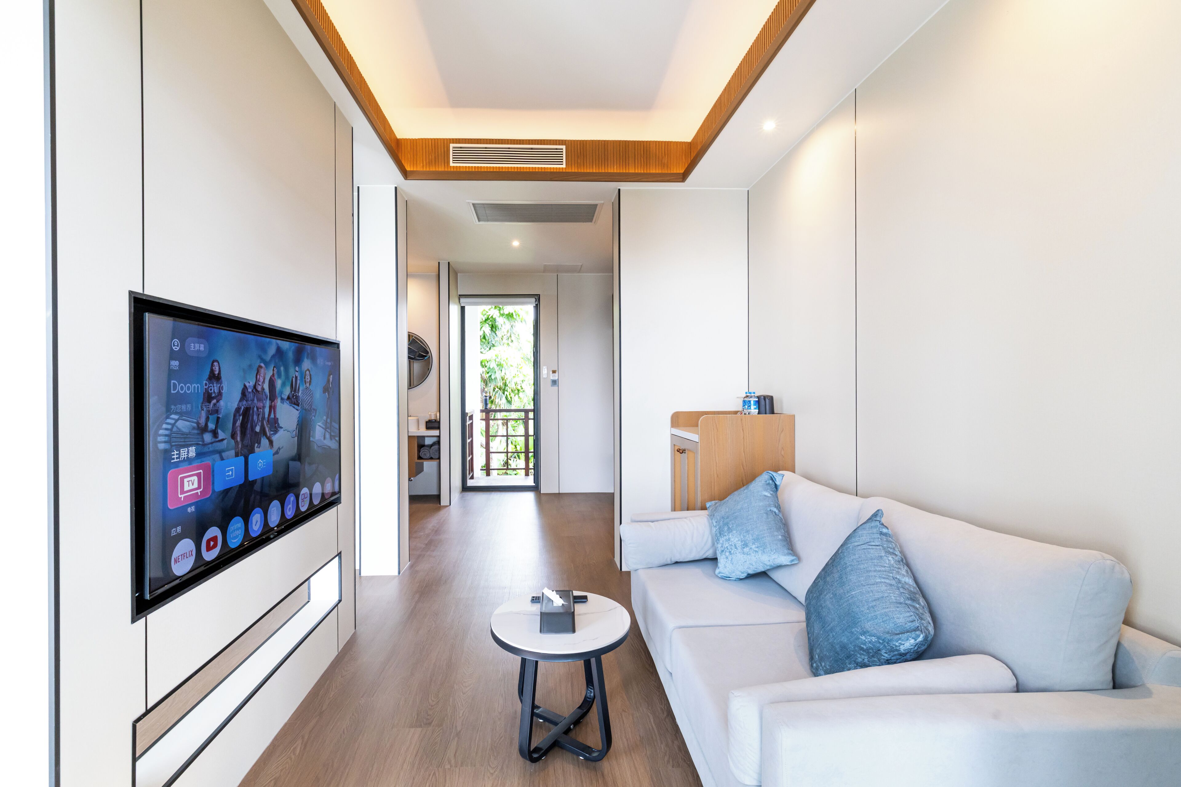 Uma sala de estar moderna com televisão de tela plana, um sofá, uma mesa de centro e vista para a cozinha e exterior.