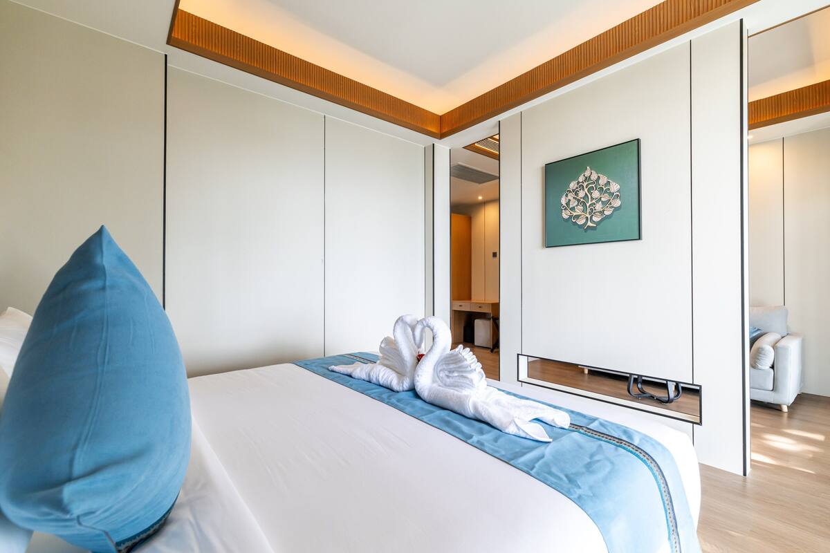 Habitación de hotel con una cama, almohada azul, una obra de arte en la pared y un espejo que refleja parte de la habitación.