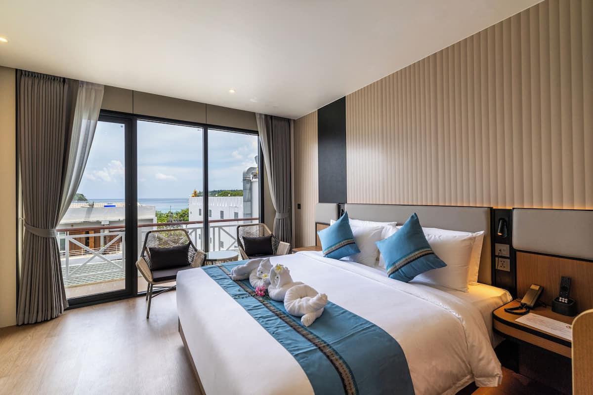 Habitación de hotel con una cama grande, una silla, una mesita de noche y vistas al mar.