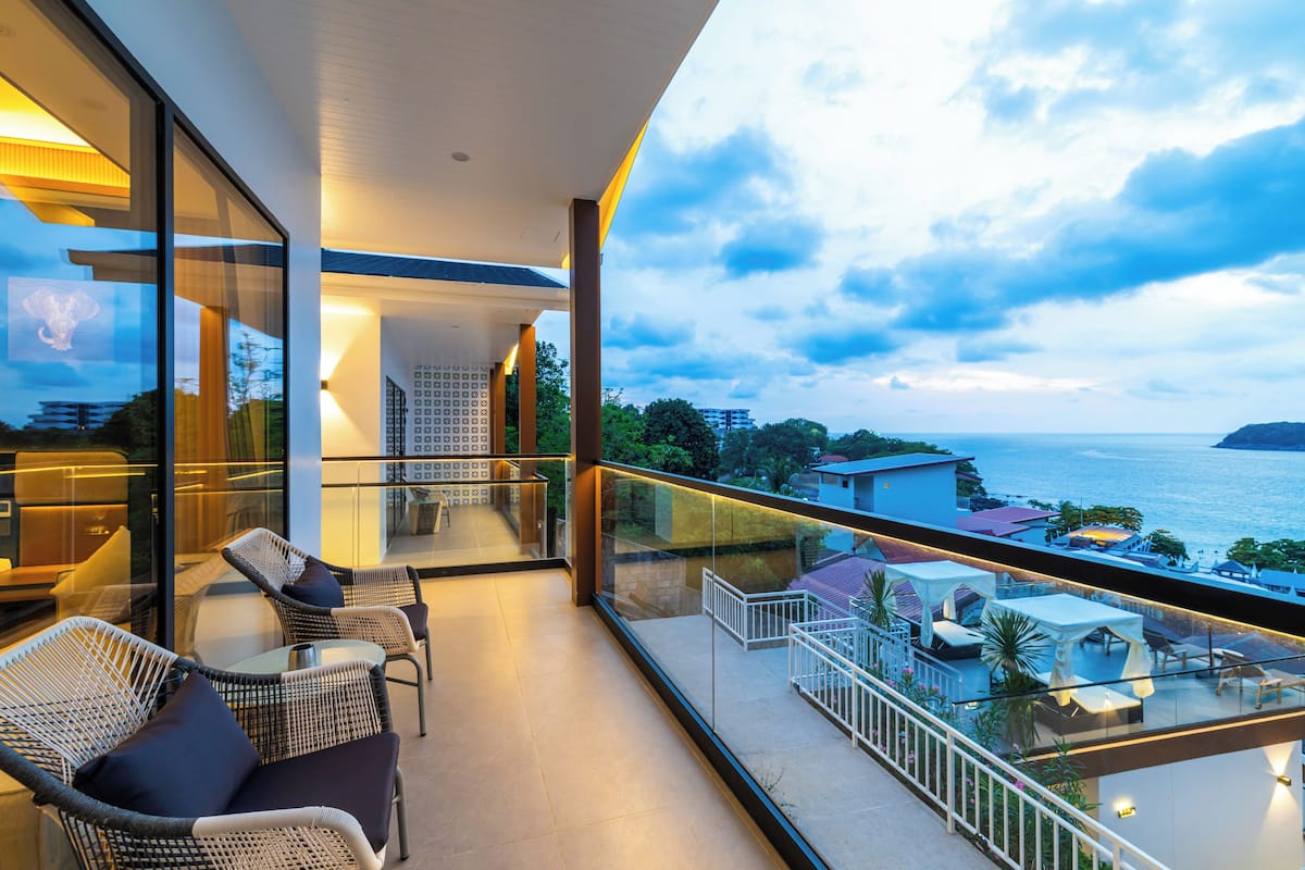 Un balcón con mobiliario de mimbre, barandilla de cristal y vista al mar.