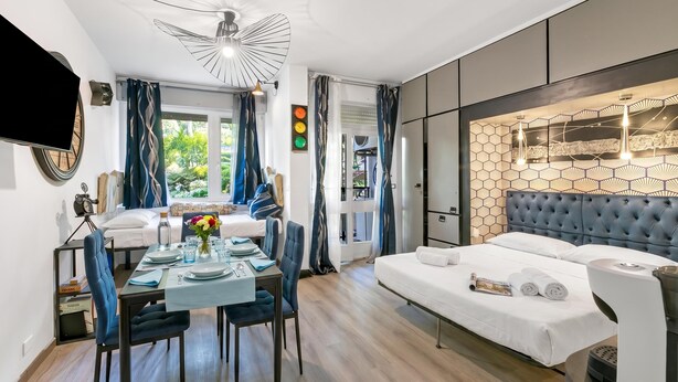 A modern hotel room with a large bed, a dining area, and a TV mounted on the wall. - Apt Suite 125 shared pool & sun terrace, Gardone Riviera, Italy (Gardone Riviera)