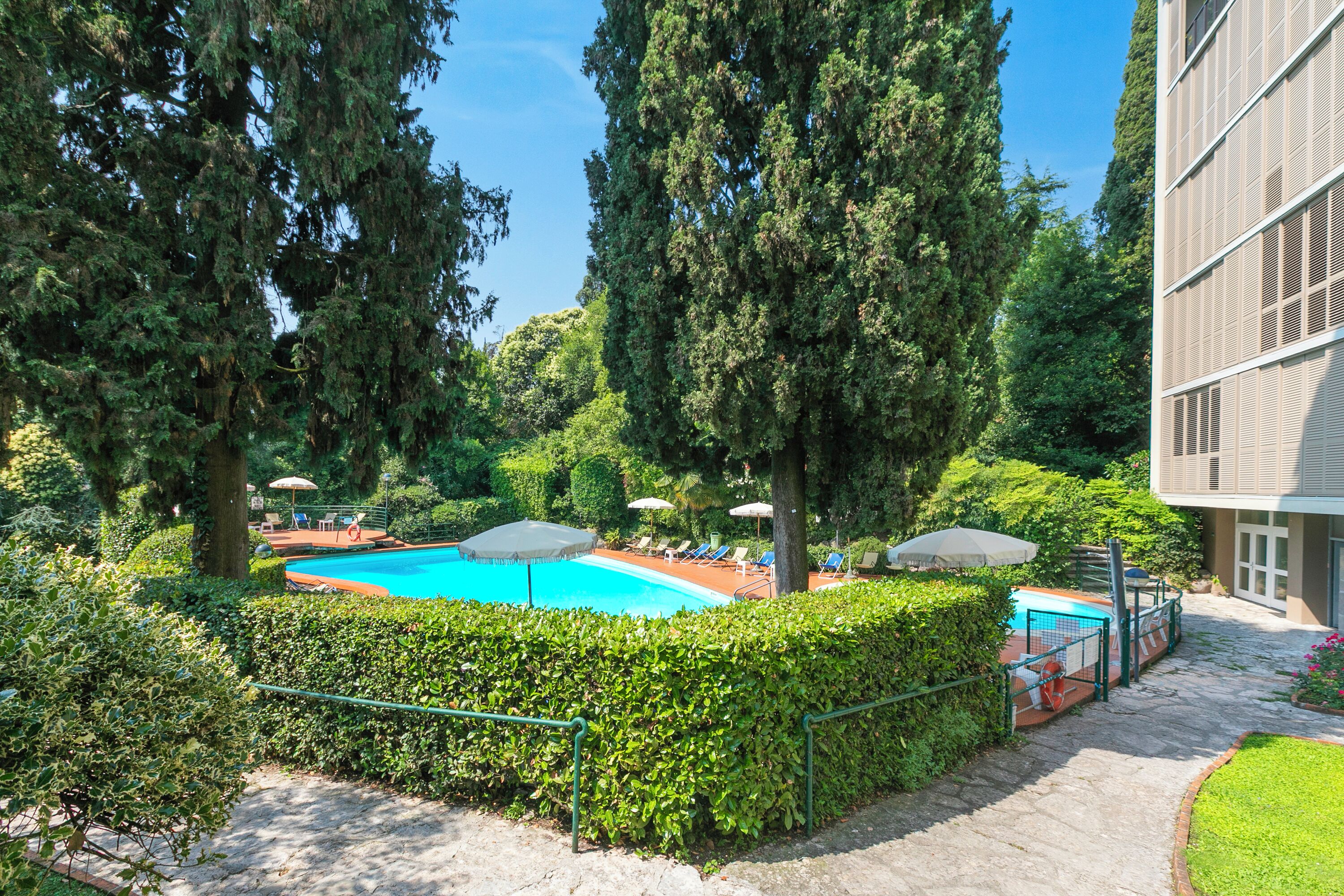 Ein Swimmingpool, umgeben von Grünflächen, ein Gebäude mit moderner Fassade und ein klarer Himmel.