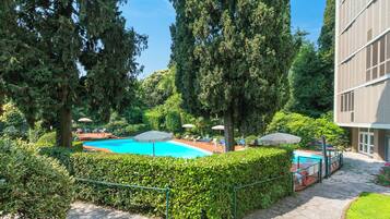 Ein Swimmingpool, umgeben von Grünflächen, ein Gebäude mit moderner Fassade und ein klarer Himmel.