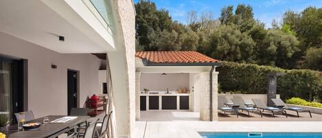 Un espace piscine extérieur moderne, aménagé avec un coin repas et un espace barbecue.