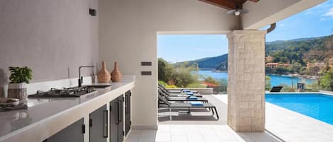 A modern kitchen with a view of a swimming pool and a scenic landscape.
