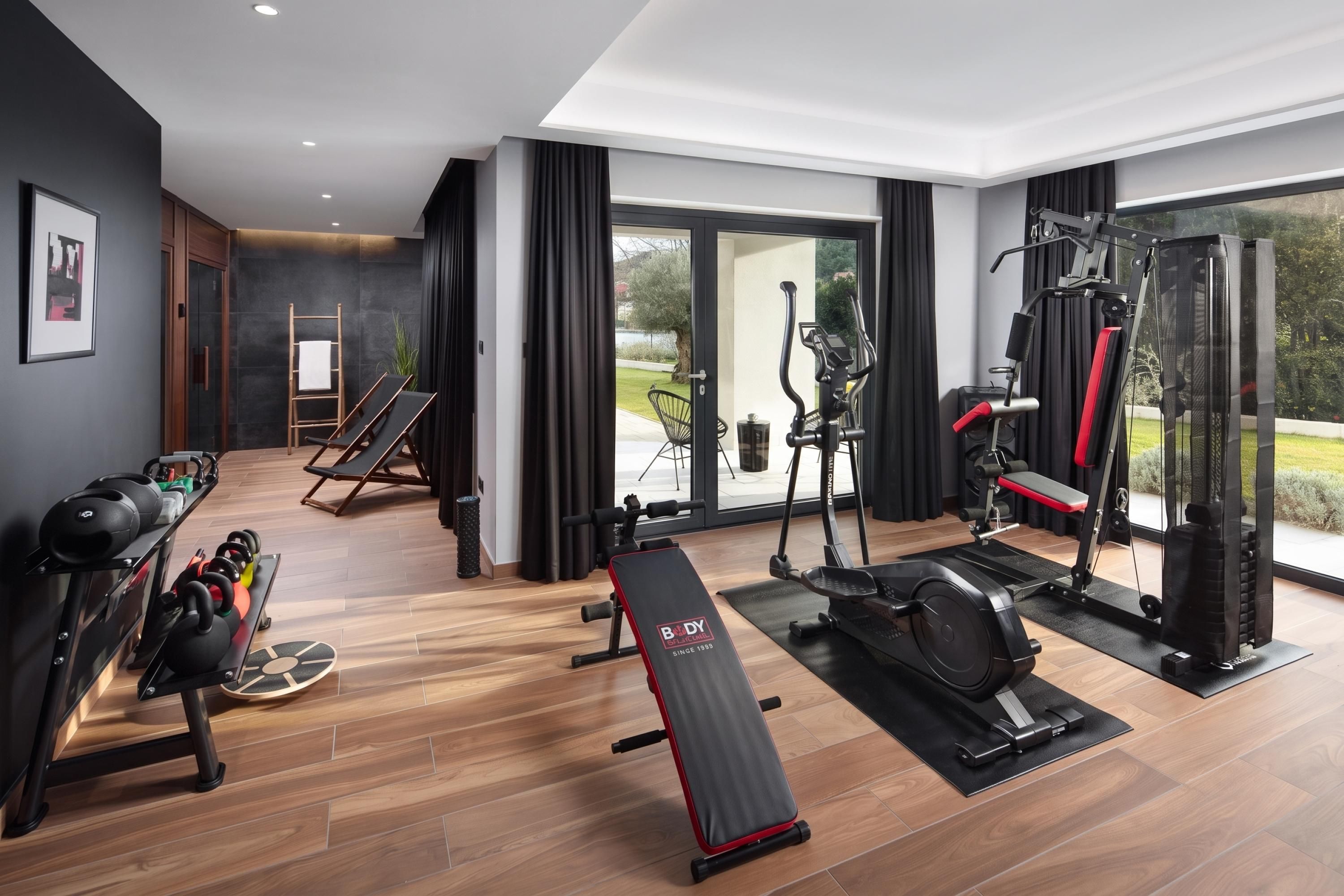 Academia moderna com equipamentos de ginástica, um banco e vista para o verde lá fora.