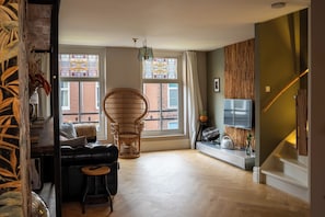 Een moderne woonkamer met een bank, een rieten fauteuil, een televisie en een trap.
