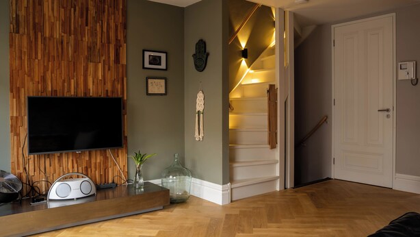 Una sala moderna con un panel de pared de madera, un televisor de pantalla plana, una radio y una escalera que lleva a un dormitorio.