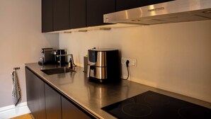 Una cocina moderna con armarios oscuros, una campana de acero inoxidable, una cafetera y una placa vitrocerámica integrada.