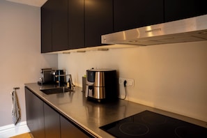 Een moderne keuken met donkere kastjes, een roestvrijstalen afzuigkap, een koffiezetapparaat en een geïntegreerd inductiekookveld.