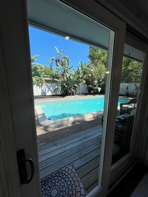 Ein Pool mit Holzterrasse, umgeben von Grünpflanzen und einem weißen Zaun.