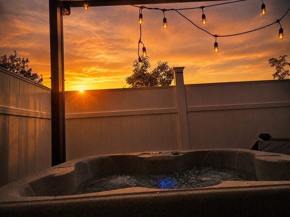A hot tub with a sunset view, surrounded by a wooden fence and string lights.
