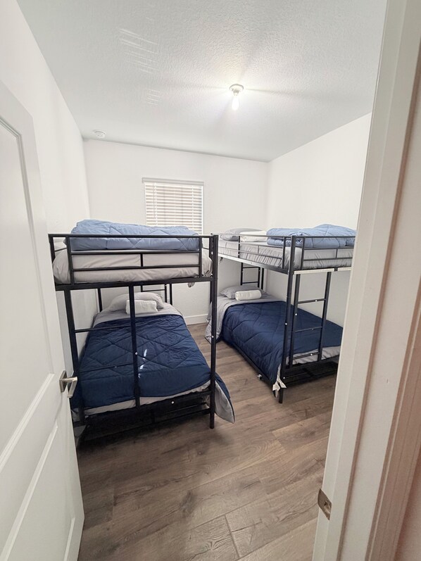 A dormitory room with bunk beds, a ceiling fan, and a window with blinds.