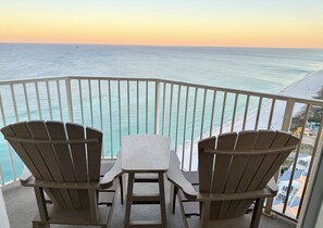 Ein Balkon mit zwei Adirondack-Stühlen und einem kleinen Tisch mit Blick auf Strand und Meer.