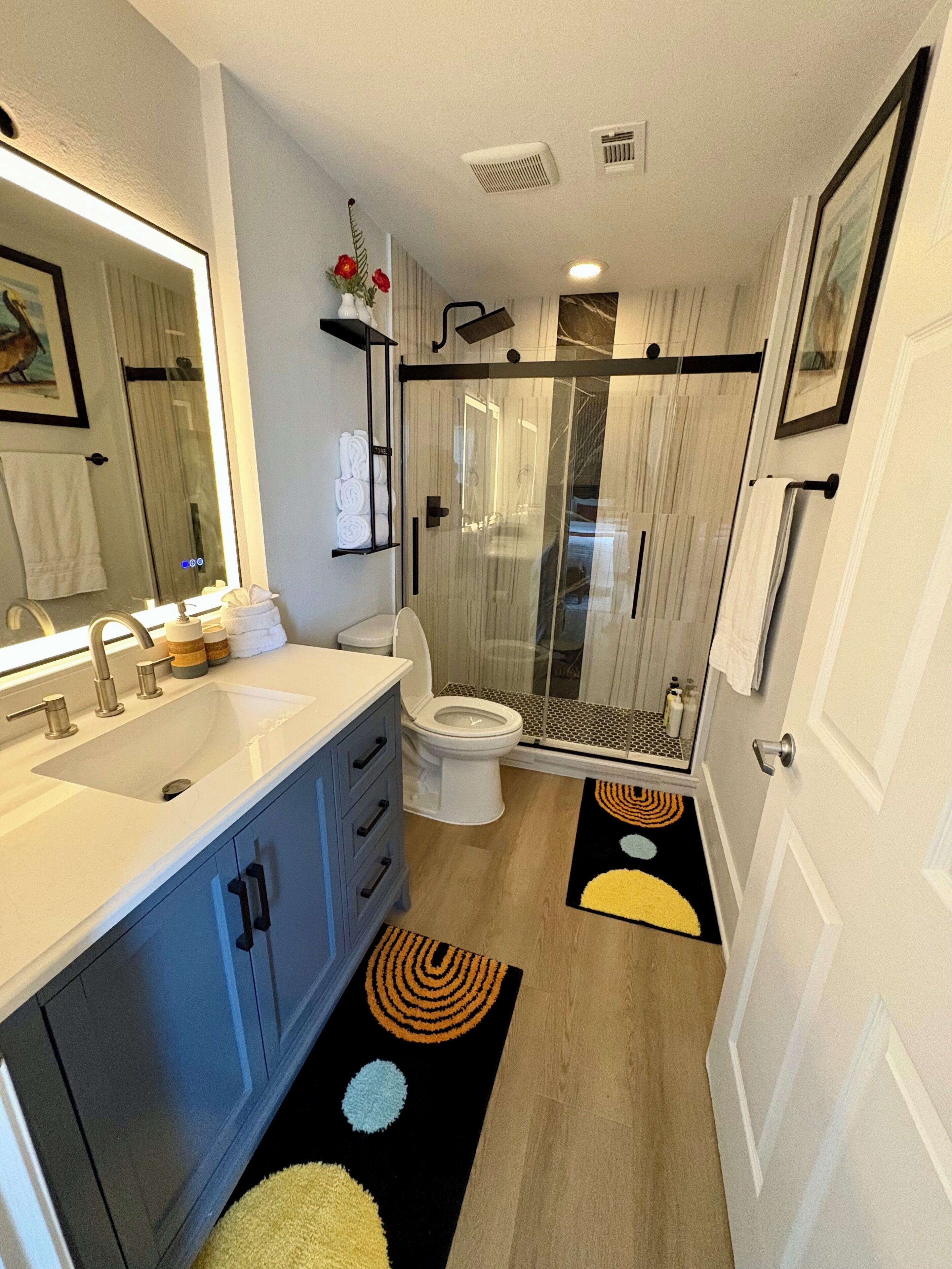 A modern bathroom with a large mirror, dual sinks, a toilet, and a glass-enclosed shower.